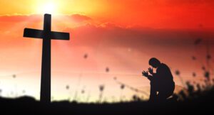 a guy praying in front of cross